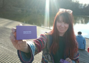 Ksenija is holding the a prototype of The Well-being Game. Behind her there's the lake.